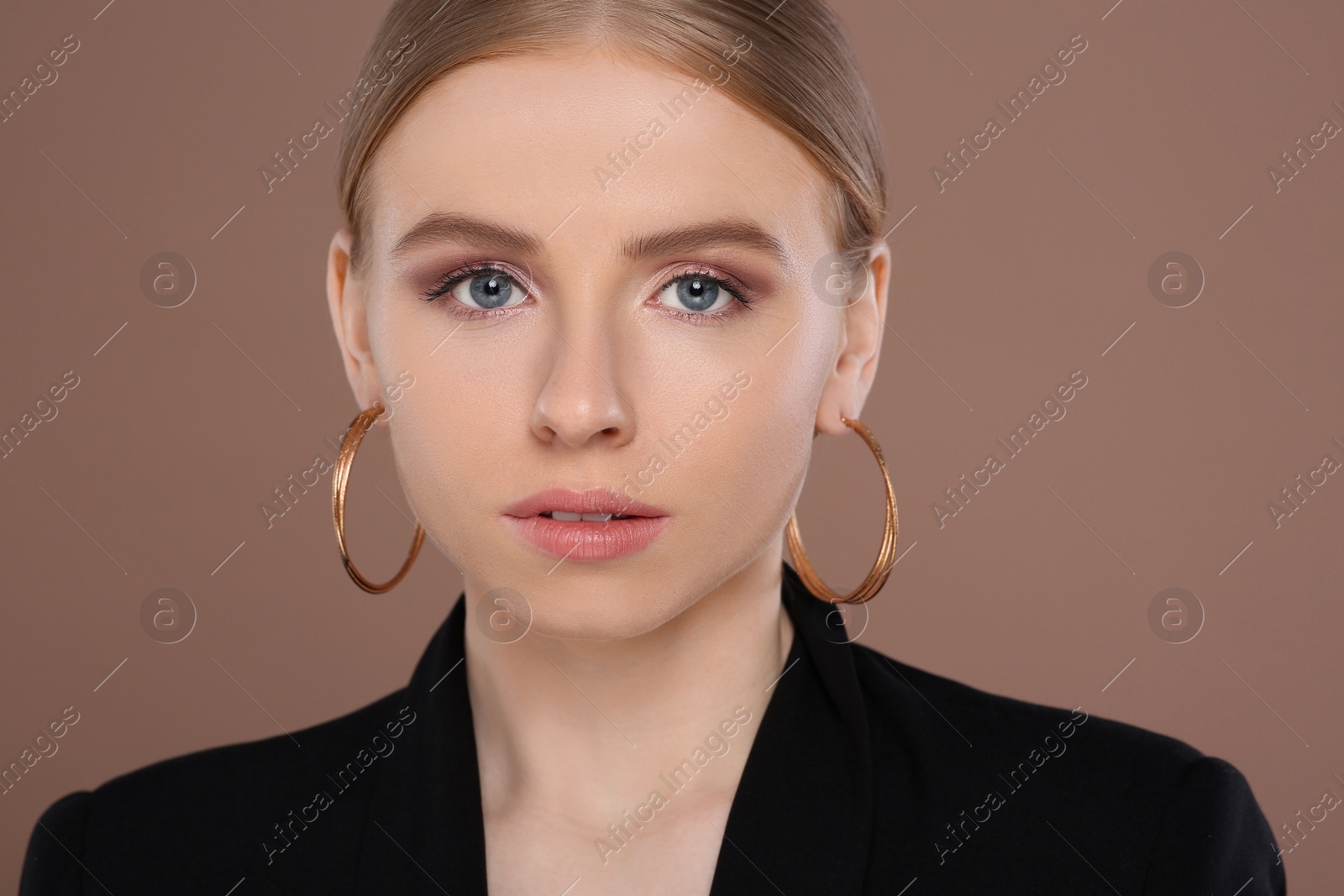 Photo of Beautiful young woman with elegant earrings on light brown background