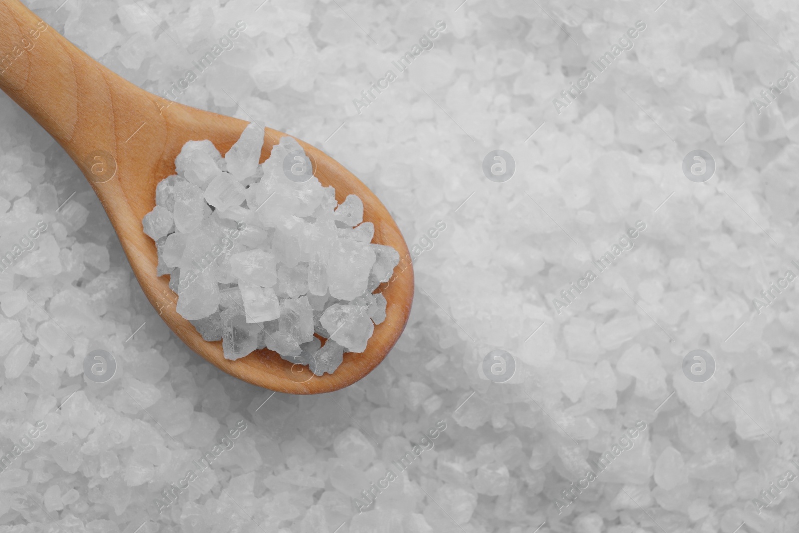 Photo of Wooden spoon with white sea salt, top view. Space for text