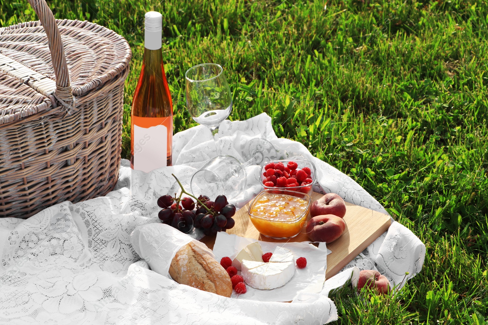 Photo of Picnic blanket with tasty food, basket and cider on green grass outdoors