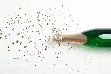 Photo of Christmas composition with bottle of champagne and shiny confetti on wooden background, top view