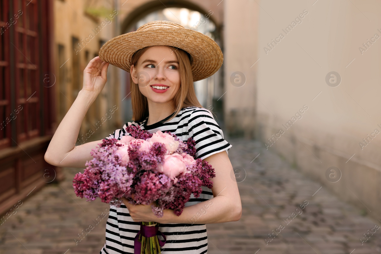 Photo of Beautiful woman with bouquet of spring flowers on city street, space for text