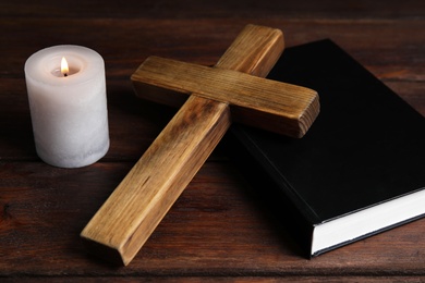 Cross, Bible and burning candle on wooden background, closeup. Christian religion