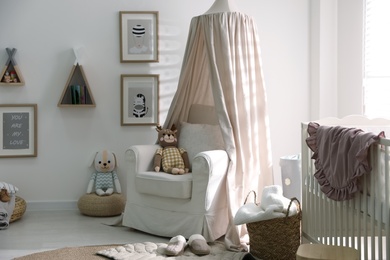 Stylish baby room interior with crib and comfortable armchair
