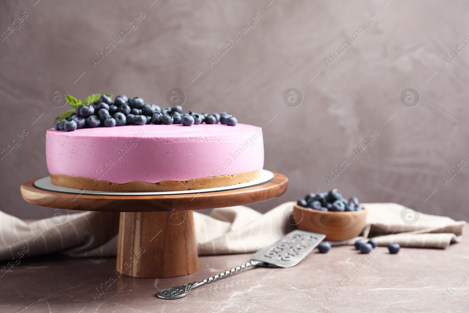 Photo of Wooden stand with tasty blueberry cake on grey table. Space for text