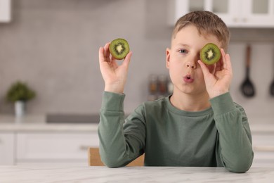 Photo of Cute boy with fresh kiwi at table in kitchen