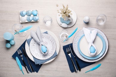 Photo of Festive table setting with bunny ears made of light blue eggs and napkins, flat lay. Easter celebration