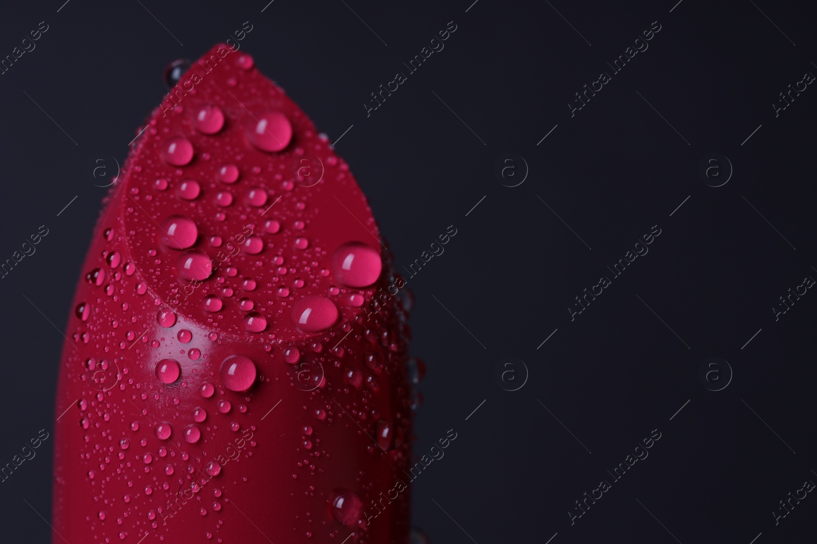 Photo of Red lipstick with water drops on dark gray background, macro view. Space for text