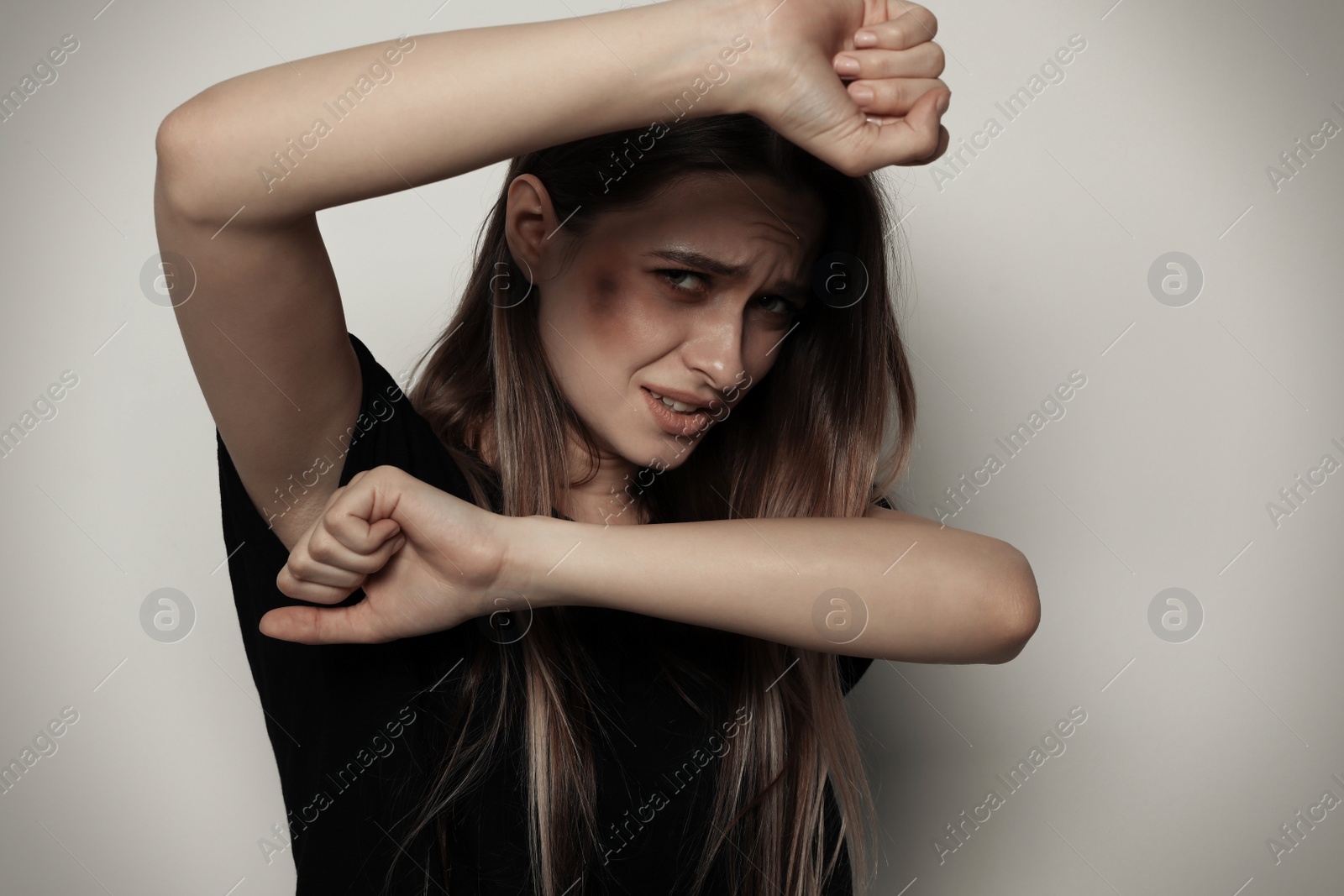 Photo of Portrait of woman protecting herself on light background. Stop violence