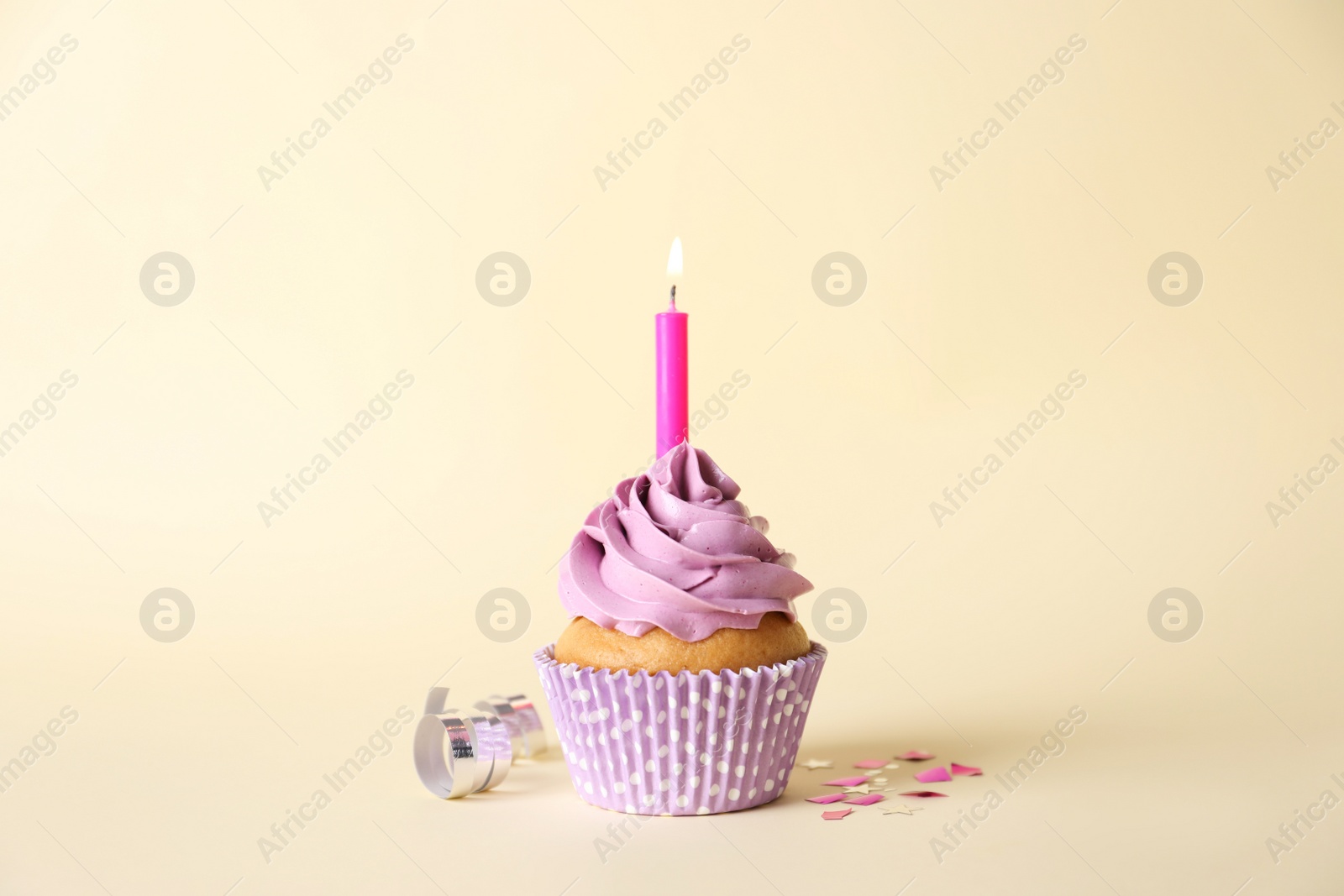 Photo of Delicious birthday cupcake with burning candle, streamer and confetti on beige background