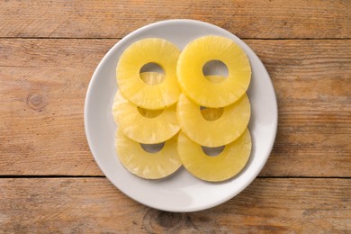 Photo of Plate with tasty canned pineapple rings on wooden table, top view