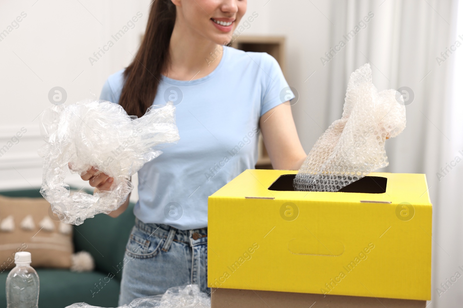 Photo of Garbage sorting. Smiling woman throwing plastic package into cardboard box in room, closeup