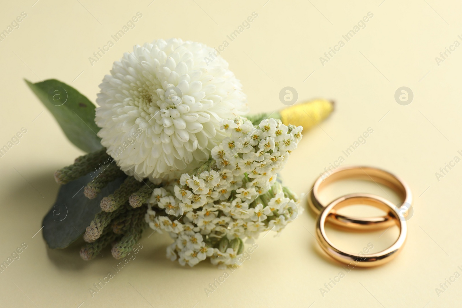 Photo of Small stylish boutonniere and rings on beige background, closeup