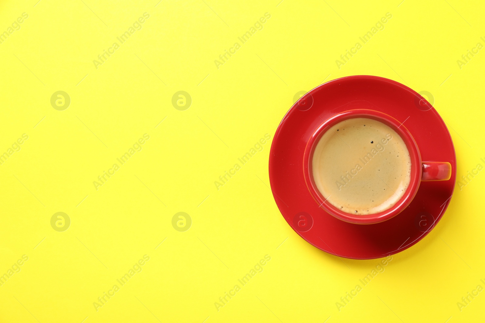 Photo of Tasty coffee in cup on yellow background, top view. Space for text