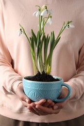 Woman holding turquoise cup with planted snowdrops, closeup