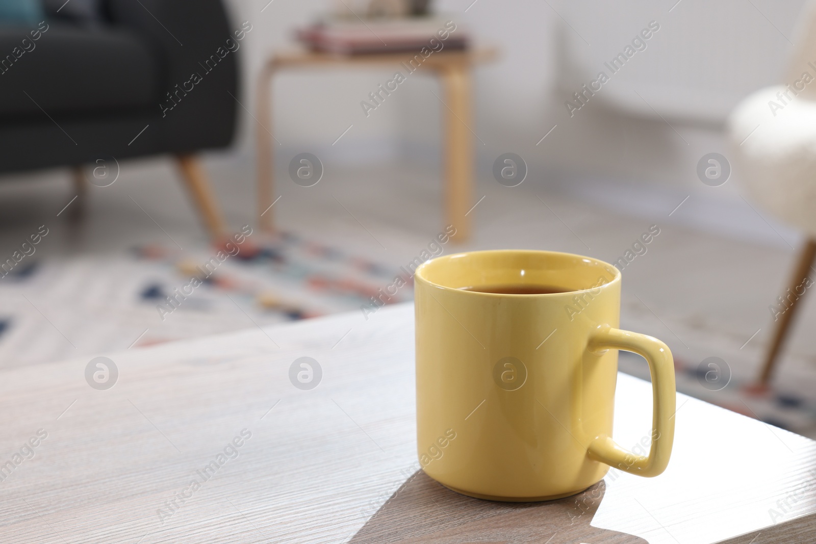 Photo of Yellow mug of tea on wooden table indoors, space for text