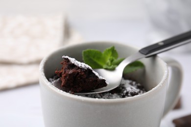 Tasty chocolate mug pie with mint and spoon on table, closeup. Microwave cake recipe