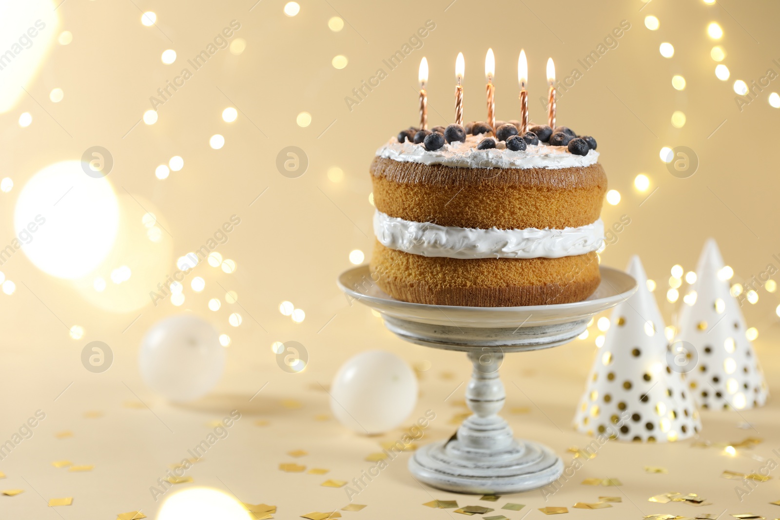 Photo of Tasty cake with burning candles on beige background against blurred lights. Space for text