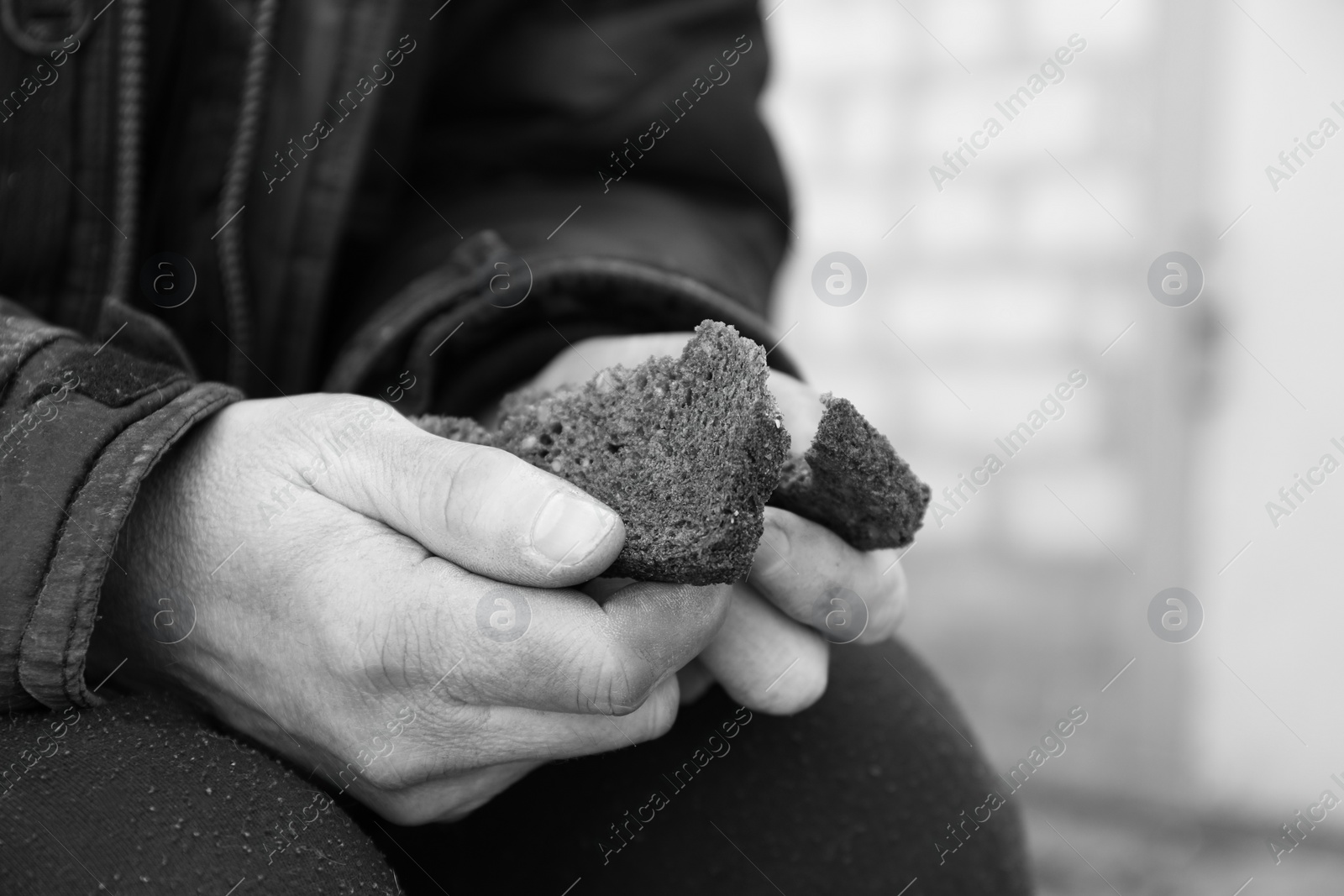 Photo of Poor homeless man holding piece of bread outdoors, closeup. Black and white effect