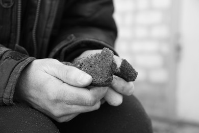 Photo of Poor homeless man holding piece of bread outdoors, closeup. Black and white effect