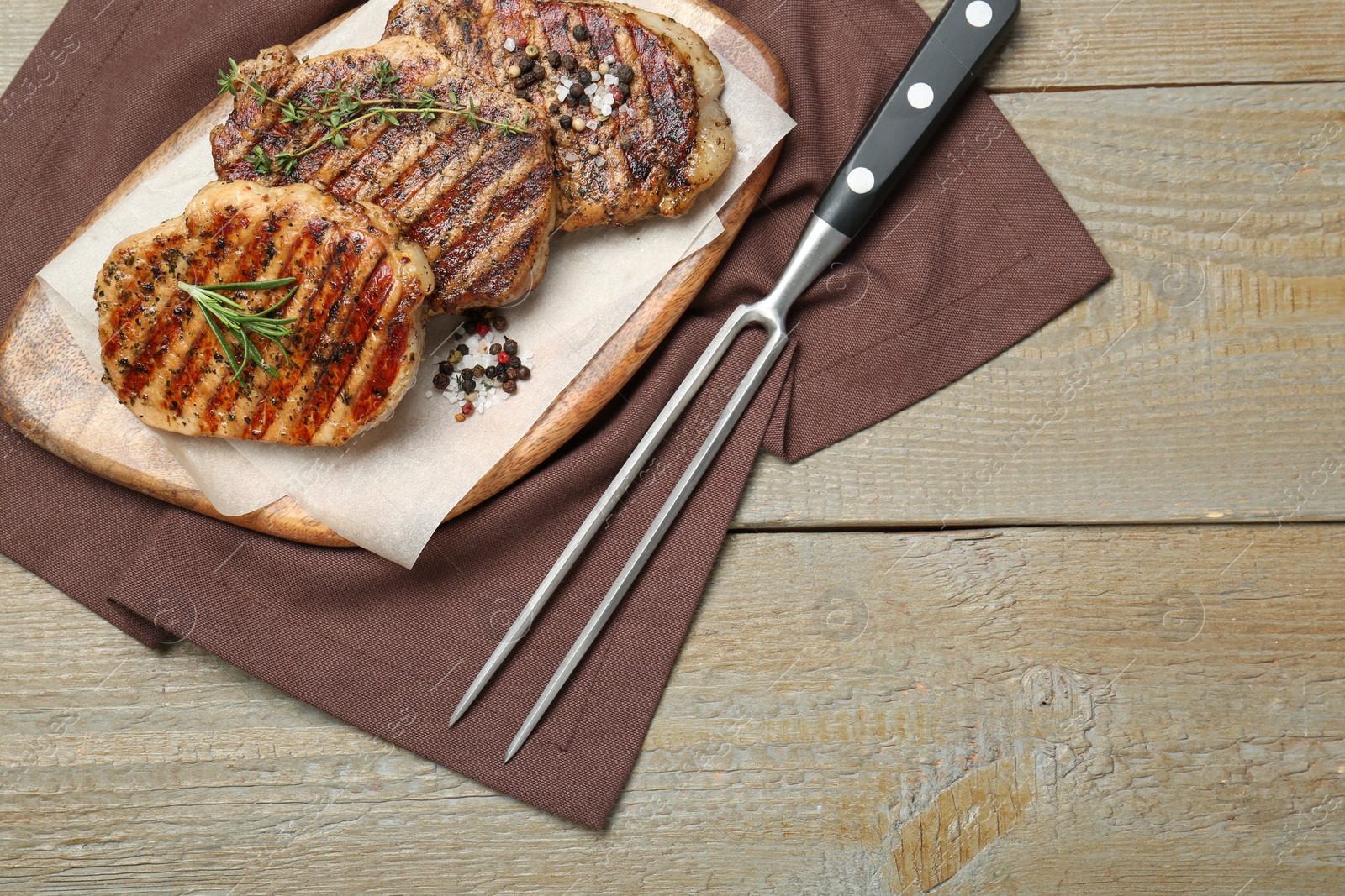 Photo of Delicious grilled pork steaks with herbs, spices and carving fork on wooden table, top view. Space for text