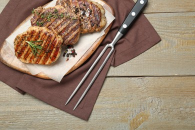 Delicious grilled pork steaks with herbs, spices and carving fork on wooden table, top view. Space for text