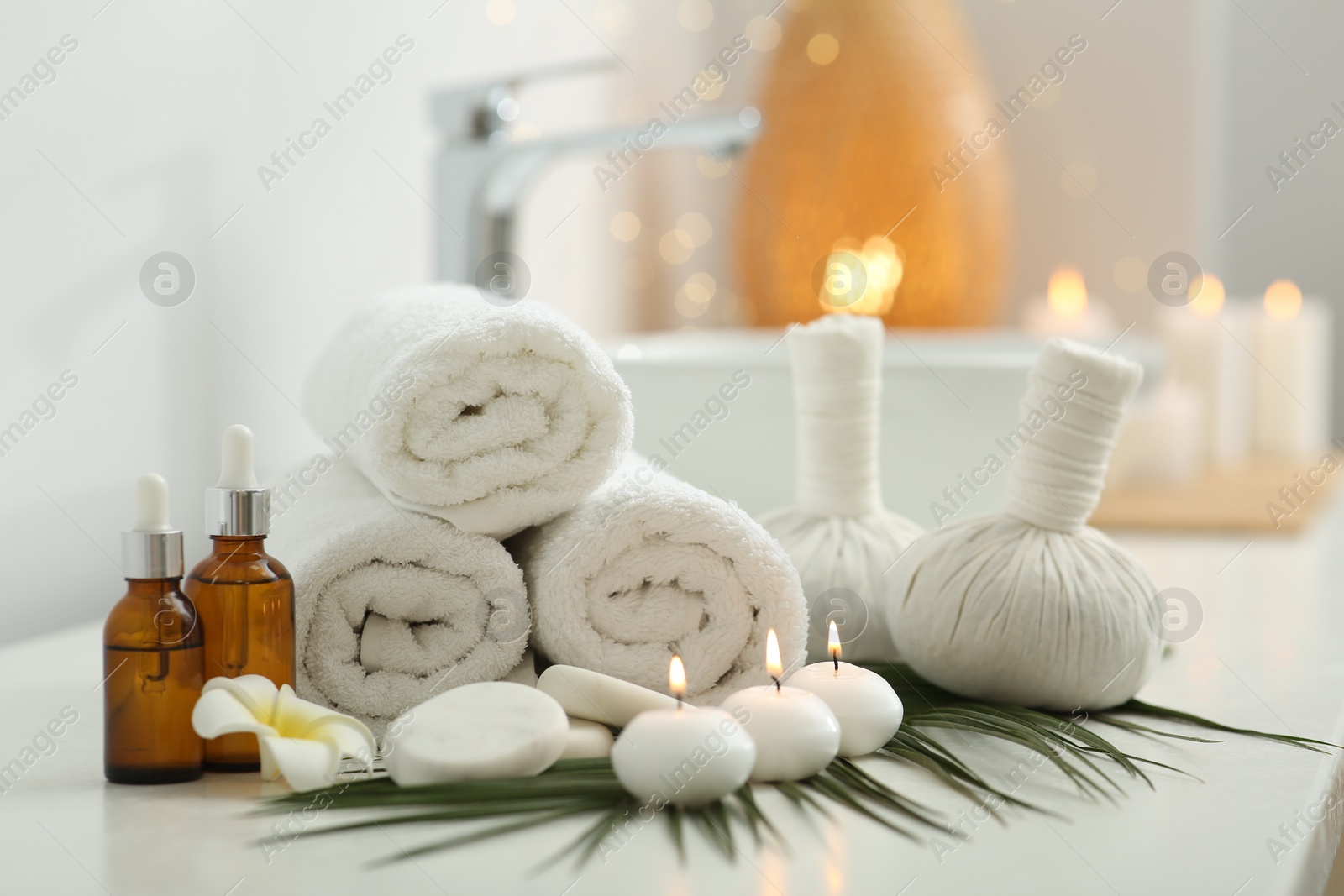 Photo of Spa composition. Rolled towels, herbal bags, cosmetic products and burning candles on white countertop in bathroom