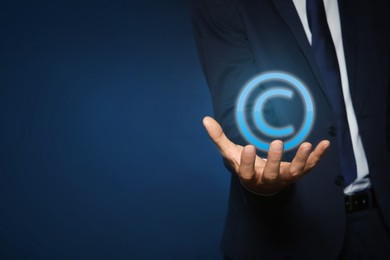 Image of Man holding virtual icon of copyright symbol on blue background, closeup. Space for text