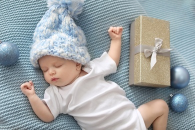 Photo of Cute baby in knitted hat with Christmas decor and gift box sleeping on blanket