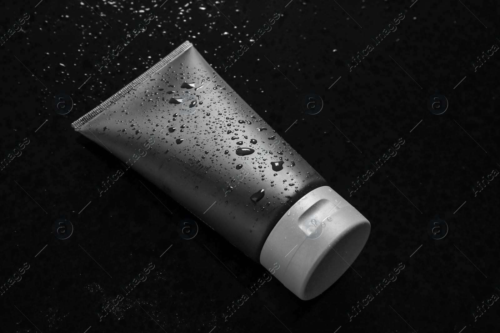 Photo of Tube on wet black surface, space for design. Men's cosmetic product