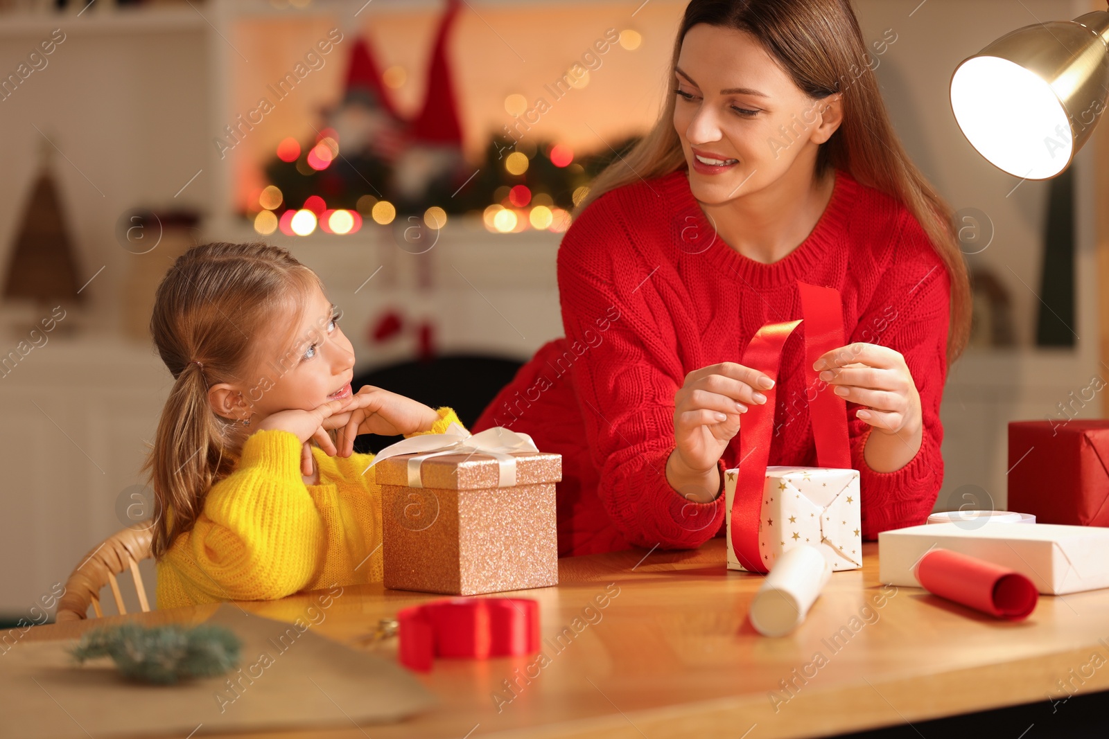 Photo of Christmas presents wrapping. Mother and her little daughter decorating gift box with ribbon at home