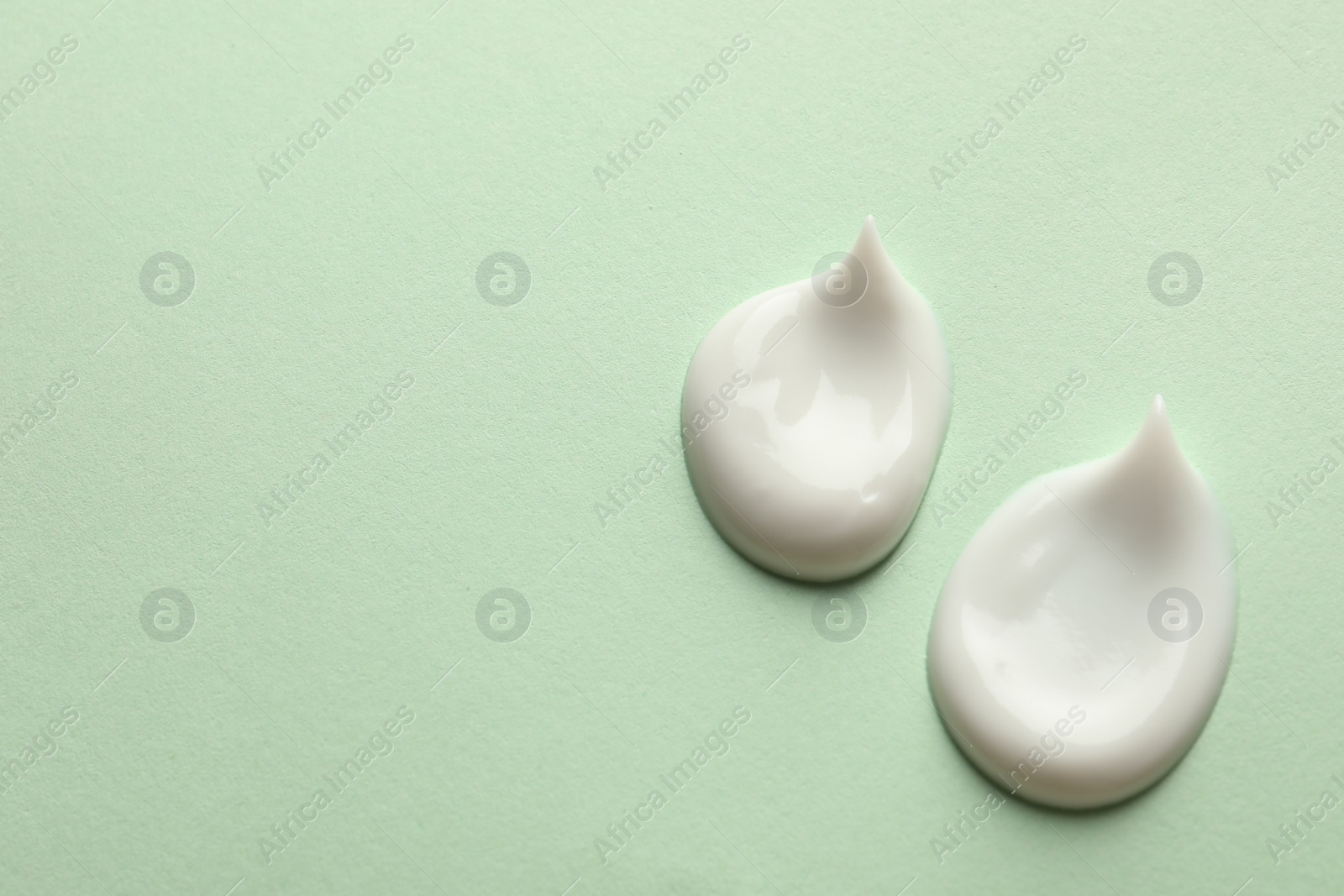 Photo of Samples of face cream on light green background, flat lay. Space for text