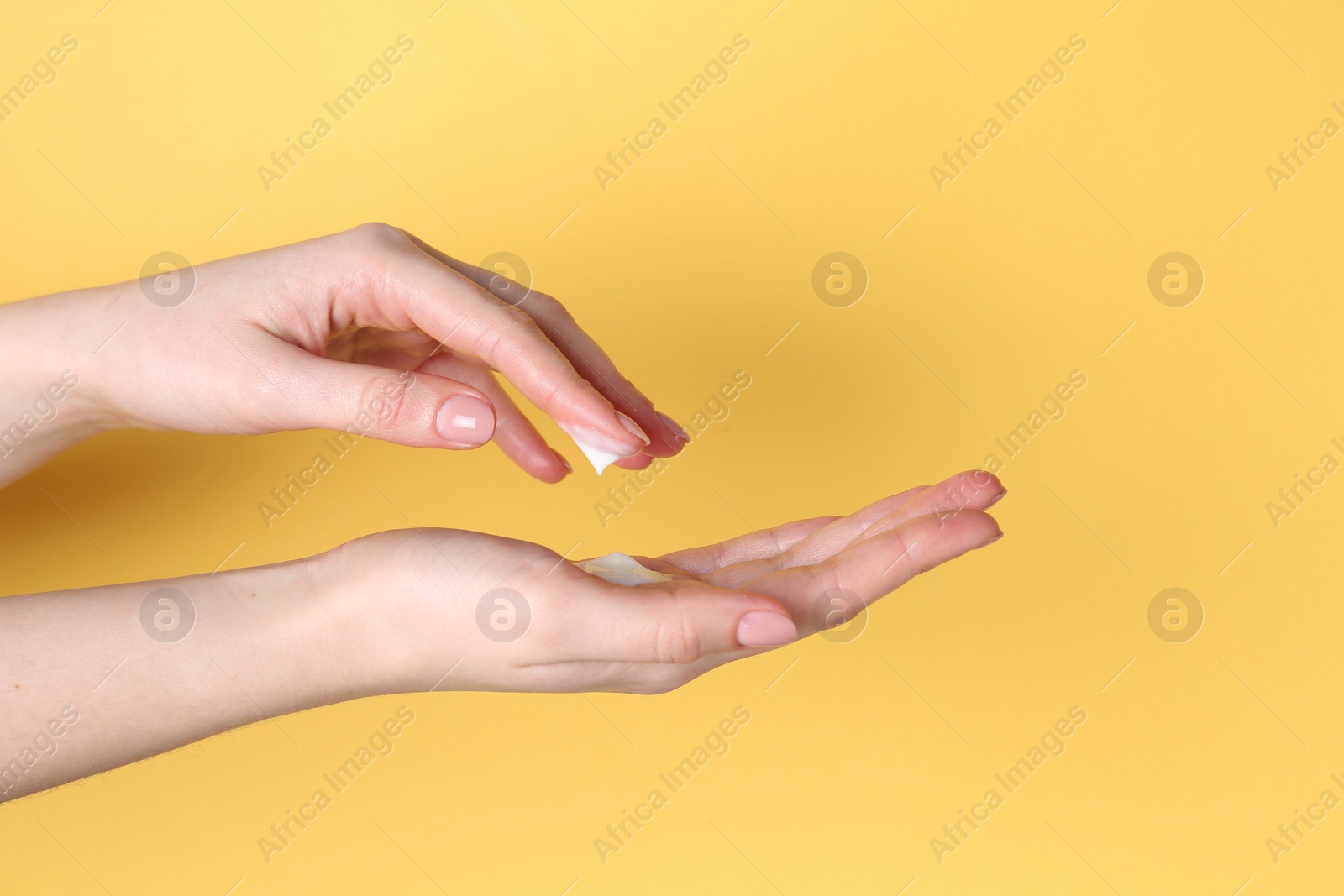 Photo of Woman applying cream on her hand against yellow background, closeup