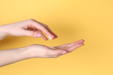 Woman applying cream on her hand against yellow background, closeup