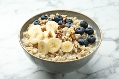 Photo of Tasty oatmeal with banana, blueberries, walnuts and milk served in bowl on white marble table