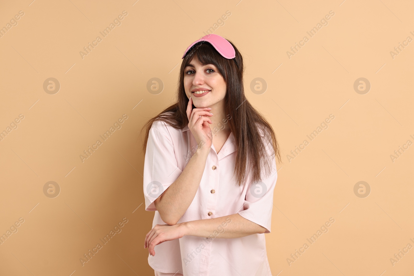 Photo of Happy woman in pyjama and sleep mask on beige background