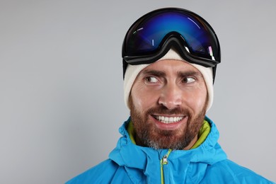 Winter sports. Happy man in ski suit and goggles on gray background, space for text