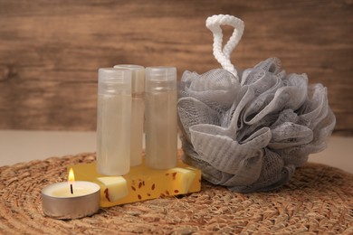 Photo of Grey shower puff, cosmetic products and candle on wicker mat, closeup