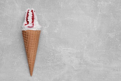 Photo of Delicious ice cream with raspberry jam in waffle cone on light gray background, top view. Space for text