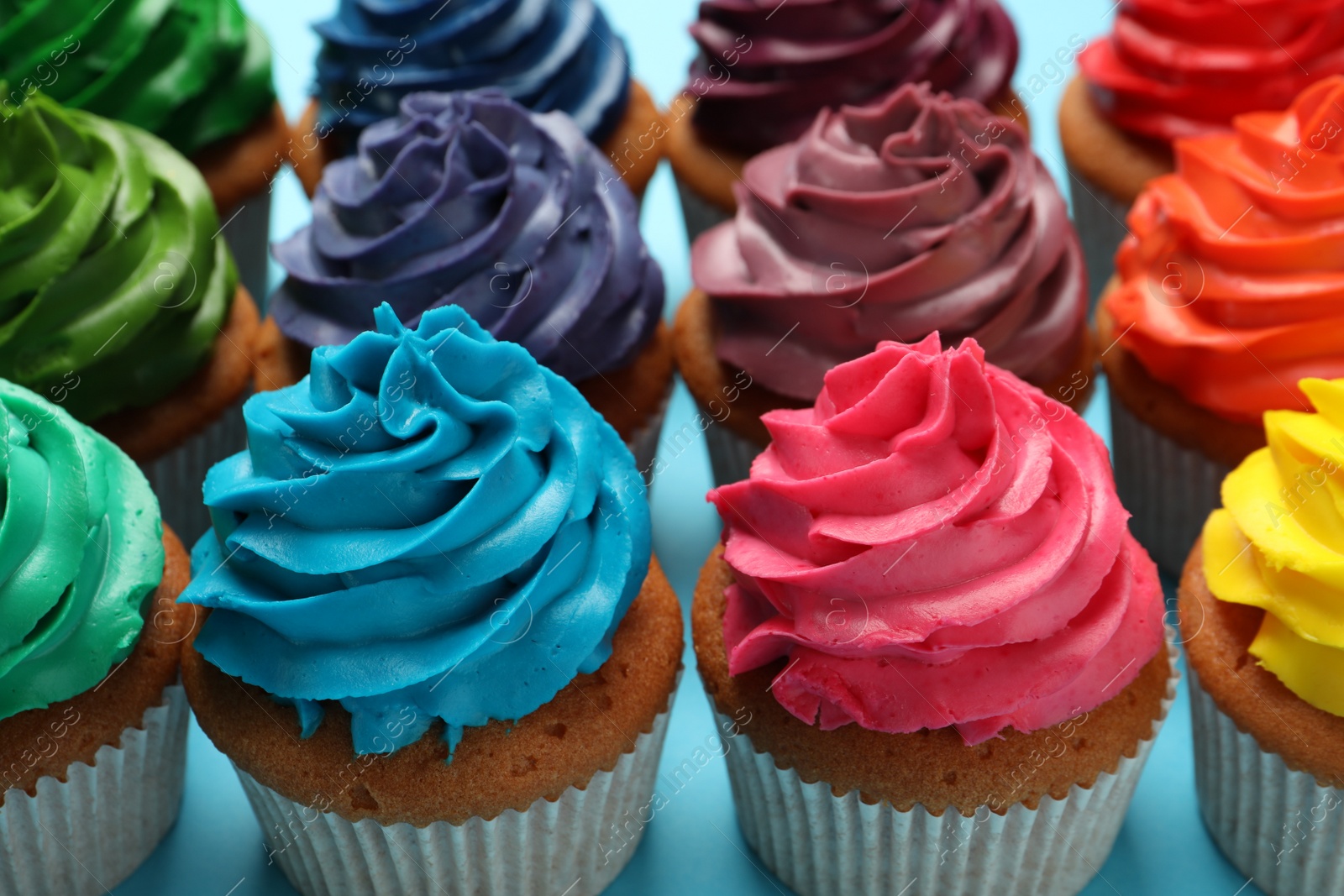 Photo of Many delicious colorful cupcakes on light blue background, closeup