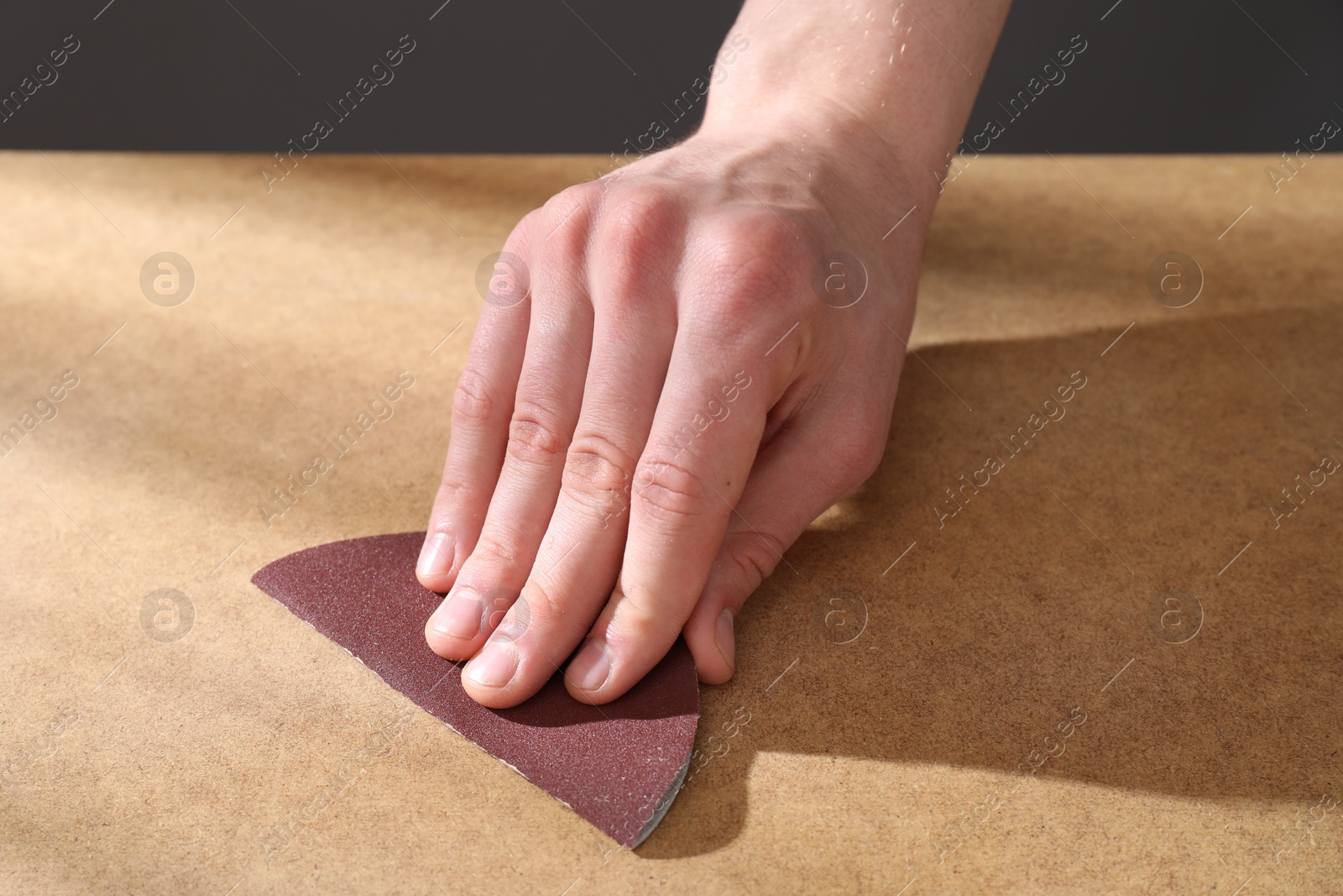 Photo of Man polishing wooden table with sandpaper, closeup