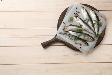 Fresh raw sprats, dill and peppercorns on light wooden table, top view. Space for text