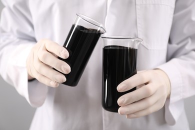 Woman pouring black crude oil into beaker on light background, closeup