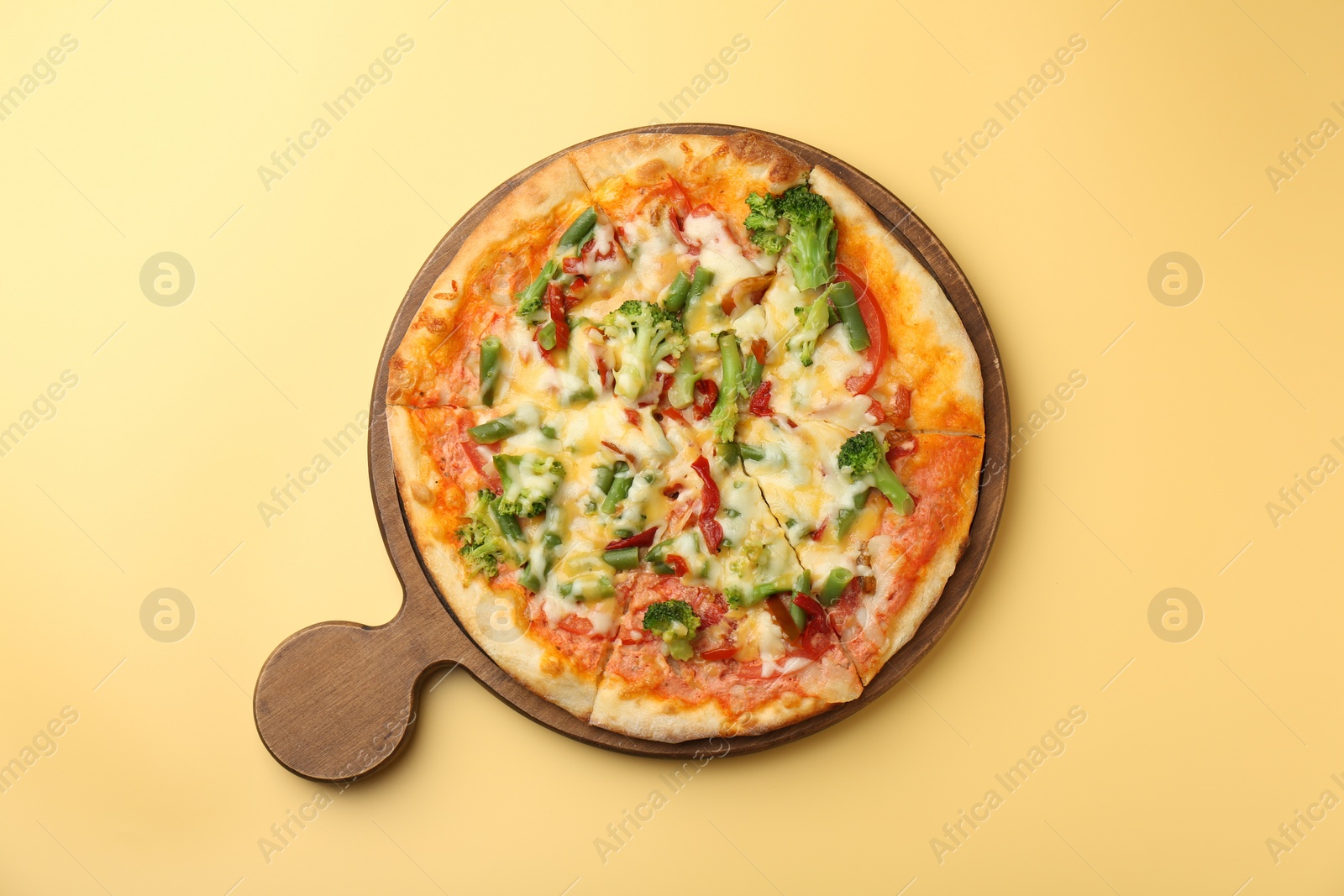 Photo of Board with delicious vegetarian pizza on yellow table, top view