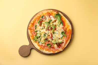 Board with delicious vegetarian pizza on yellow table, top view