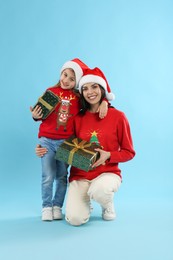 Photo of Mother and daughter with Christmas gifts on light blue background
