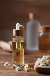 Photo of Bottle of chamomile essential oil and flowers on wooden table