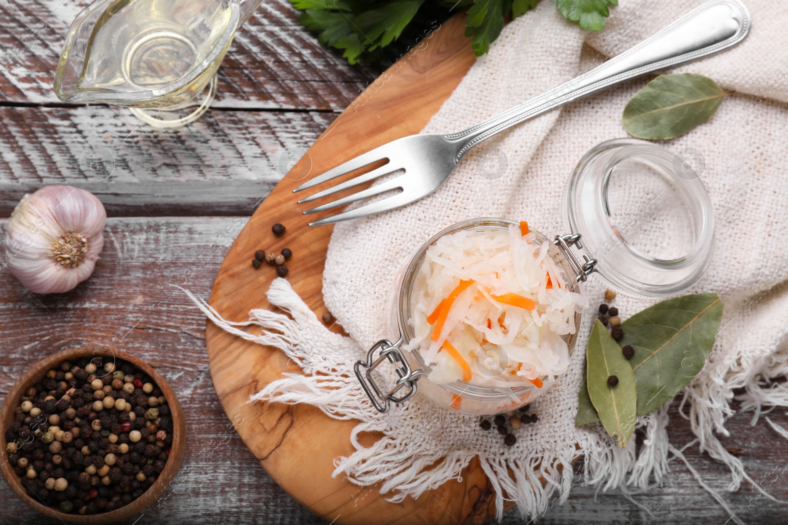 Photo of Glass jar of tasty sauerkraut and ingredients on wooden table, flat lay