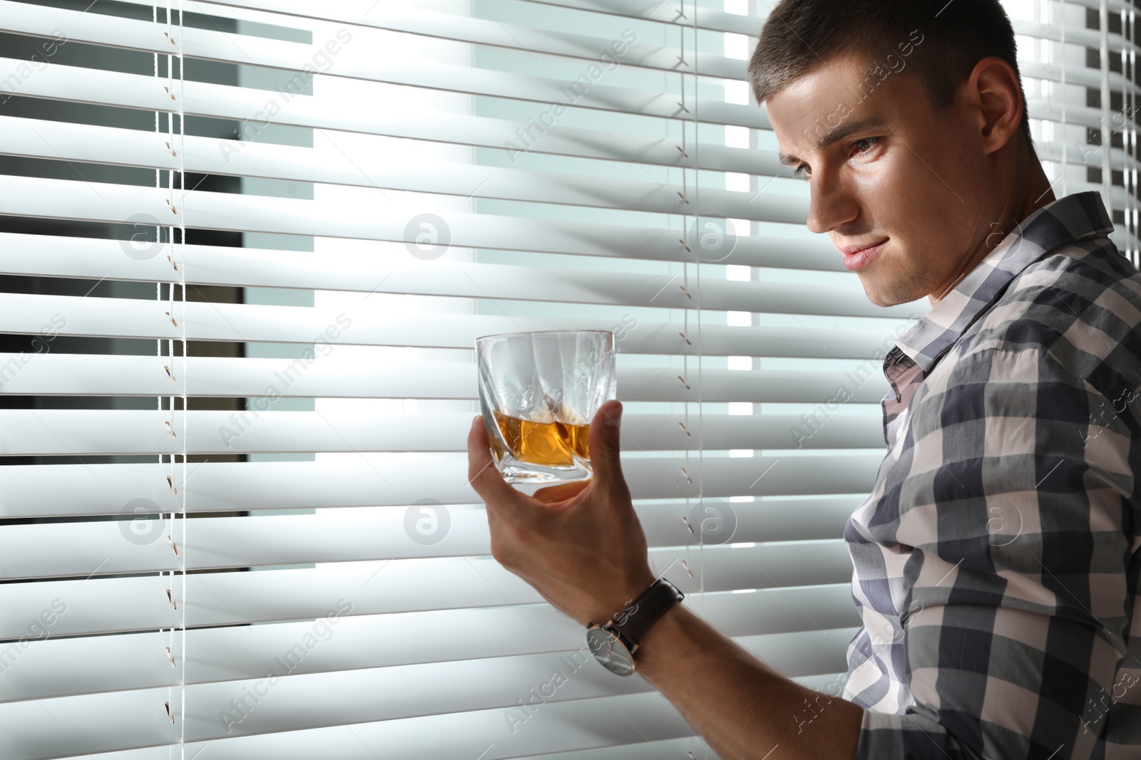 Photo of Young man with glass of whiskey near window indoors. Space for text