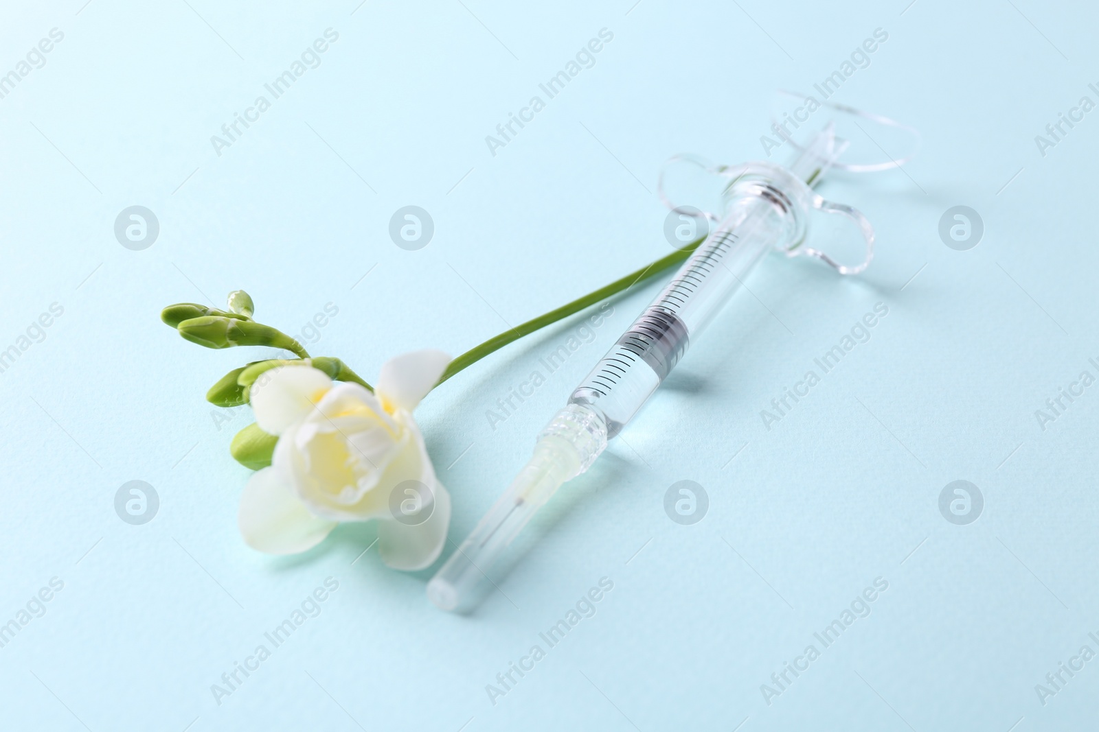 Photo of Cosmetology. Medical syringe and freesia flower on light blue background, closeup
