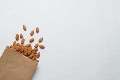 Paper bag with delicious almonds on white background, top view. Space for text